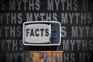 TV with green screen on wood furniture in front of a blackboard. The word "facts" is shown on the screen among many words "myths" written on the blackboard